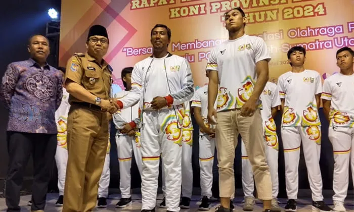 Asisten 1 Setdaprov Khairil Anwar mengenakan baju seragam Pelatda kepada atlet pada acara Rakerprov.(foto/tarmandi)
